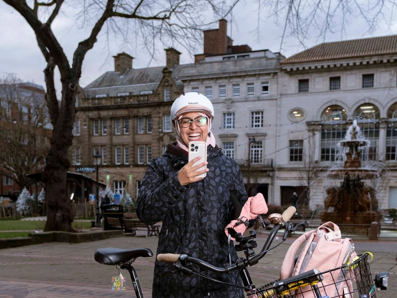 Sarah M. Jasat steht mit ihrem Rad auf einem Platz in Leicester und lacht ins Handy