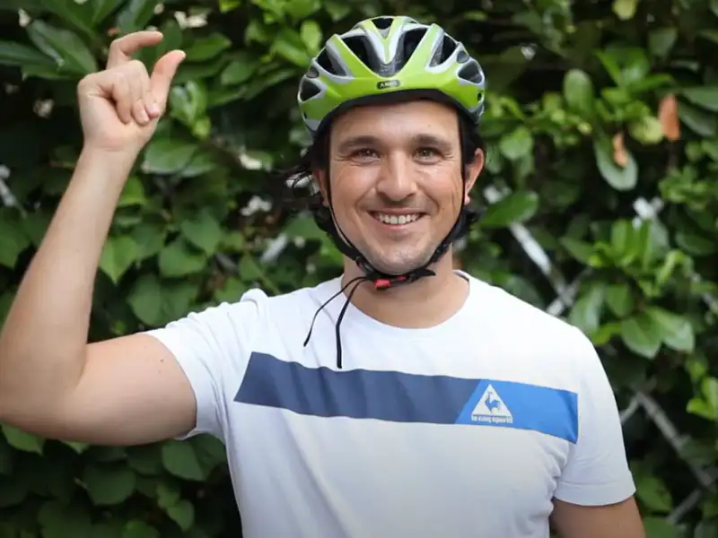 Ein American Express Mitarbeiter mit grünem Fahrradhelm vor einer grünen Hecke Ein American Express Mitarbeiter mit grünem Fahrradhelm vor einer grünen Hecke