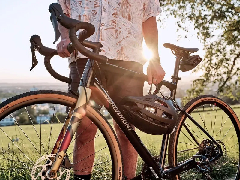 Close Up auf einen Mann, der ein neues Gravelbike hält, er steht auf einer Sonnendurchfluteten Wiese